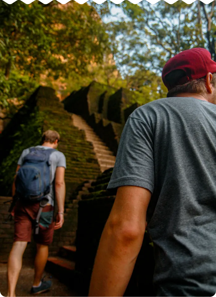 Two hikers climbing moss-covered stone steps through a forest